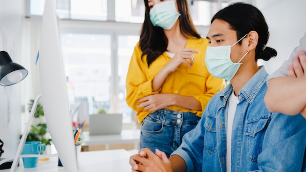 Kostenloses Foto geschäftsleute aus asien, die computerpräsentationen verwenden, treffen sich mit brainstorming-ideen über neue projektkollegen und tragen eine schützende gesichtsmaske in einem neuen normalen büro. lebensstil und arbeit nach coronavirus.