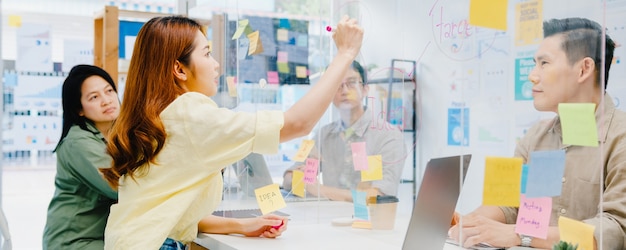 Kostenlose Foto geschäftsleute aus asien, die gemeinsam über ein business-brainstorming-meeting diskutieren, tauschen daten aus und schreiben auf eine acryl-partition. sie treten in einem neuen normalen büro zurück. lebensstil soziale distanzierung und arbeit nach coronavirus.