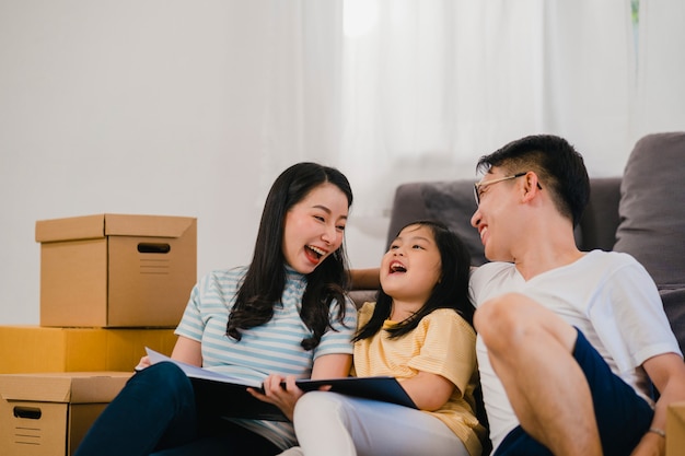 Kostenloses Foto glückliche asiatische junge familienhausbesitzer kauften neues haus. chinesische mutter, vati und tochter, die das vorwärtsschauen zur zukunft im neuen haus umfassen, nachdem sie in den umzug umgezogen sind, der zusammen auf boden mit kästen sitzt.