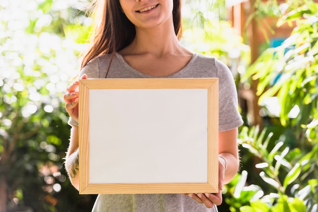 Kostenloses Foto glückliche frau, die fotorahmen zwischen anlagen hält