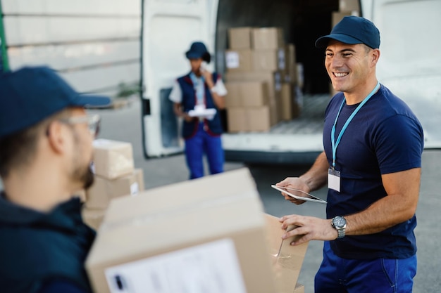 Kostenloses Foto glücklicher arbeiter, der touchpad verwendet, während er mit seinem kollegen kommuniziert und die paketzustellung organisiert