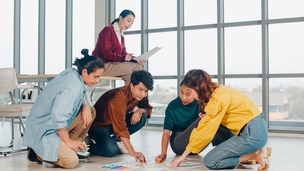 Kostenloses Foto gruppe asiatischer junger kreativer leute in der freizeitkleidung, die geschäfts-brainstorming-besprechungsideen diskutiert, die designplan des mobilen anwendungssoftwareentwurfs auf boden im büro angelegt werden. teamwork-konzept für mitarbeiter.