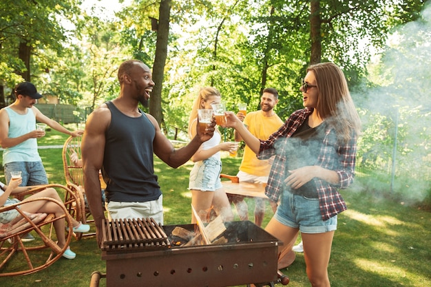 Kostenloses Foto gruppe von glücklichen freunden, die bier und grillparty am sonnigen tag haben. zusammen im freien in einer waldlichtung oder im hinterhof ausruhen