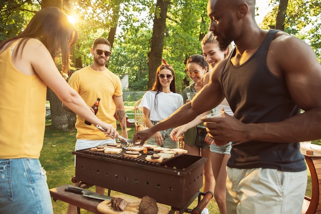 Kostenloses Foto gruppe von glücklichen freunden, die bier und grillparty am sonnigen tag haben. zusammen im freien in einer waldlichtung oder im hinterhof ausruhen