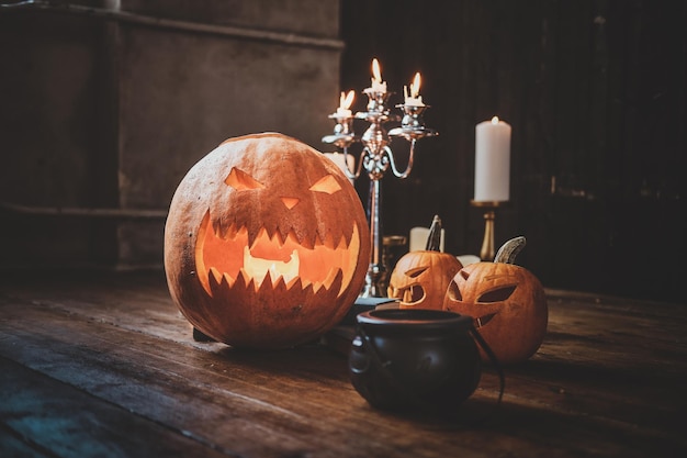 Halloween traditionell geschnitzte Kürbisse, kleiner Kessel und Kerzen auf dem Holzboden.