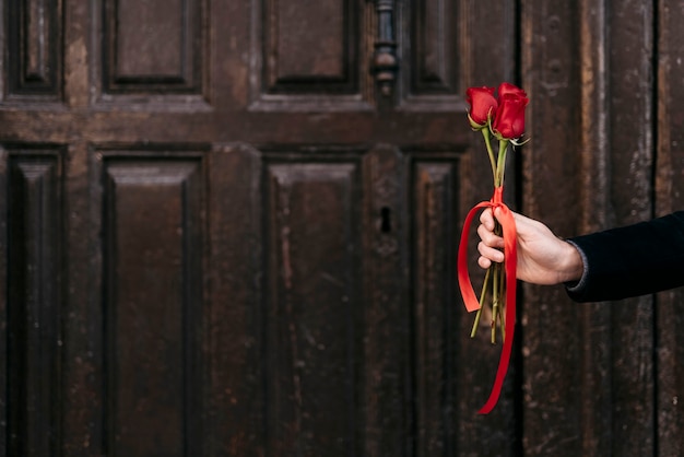 Hand, die seinem Paar roten Rosenstrauß mit Kopierraum gibt