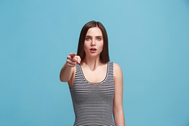 Ich wähle dich und bestelle. Die überraschte Frau zeigt Sie, will Sie, Nahaufnahmeporträt in halber Länge auf blauem Studiohintergrund. Die menschlichen Emotionen, Gesichtsausdruckkonzept. Vorderansicht. Trendige Farben