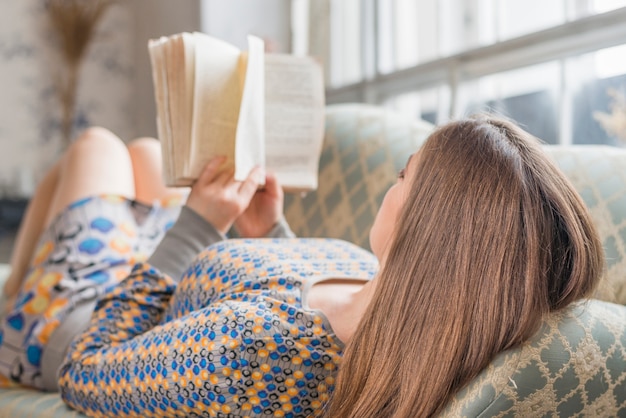 Kostenloses Foto junge frau, die auf sofalesebuch liegt