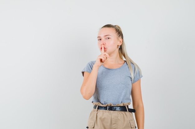 Kostenloses Foto junge frau, die stille geste im t-shirt, in der hose zeigt und vorsichtig schaut, vorderansicht.