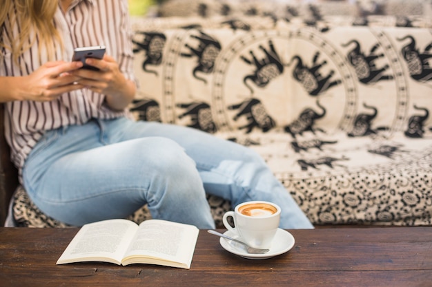 Kostenloses Foto kaffeetasse und offenes buch vor der frau, die handy verwendet