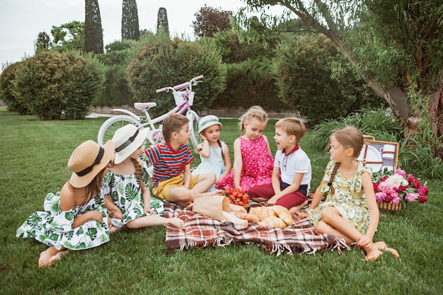 Kostenloses Foto kindermode-konzept. gruppe von jugendlichen jungen und mädchen, die am grünen gras am park sitzen