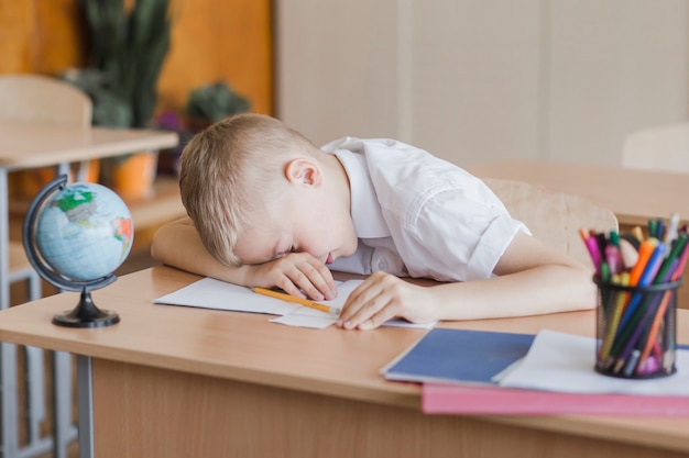 Kleiner Schüler, der auf Tabelle im Klassenzimmer legt