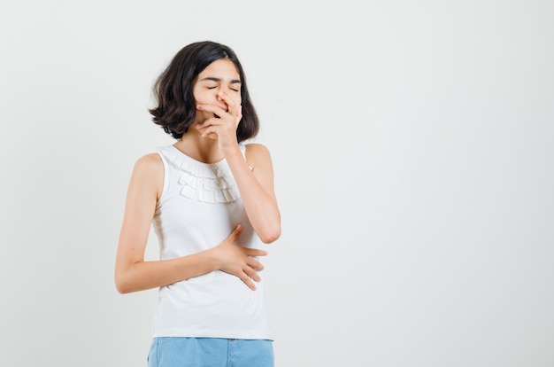 Kostenloses Foto kleines mädchen in der weißen bluse, shorts, die gähnen und schläfrig aussehen, vorderansicht.