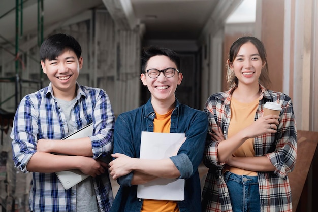 Kostenloses Foto lächelnde asiatische teamarbeit junger innendesigner-porträts stehen zusammen, handbrust, selbstbewusstes und intelligentes team mit hintergrund der baurenovierung