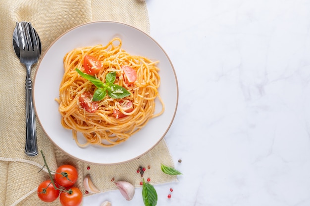 Kostenloses Foto leckere appetitliche klassische italienische spaghetti-nudeln mit tomatensauce, käseparmesan und basilikum auf dem teller und zutaten zum kochen von nudeln auf weißem marmortisch. flache draufsicht kopienraum.