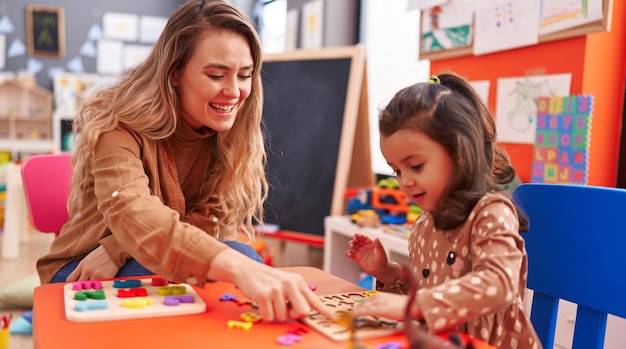 Kostenloses Foto lehrer und kleinkind spielen mit mathe-puzzle-spiel auf dem tisch im kindergarten