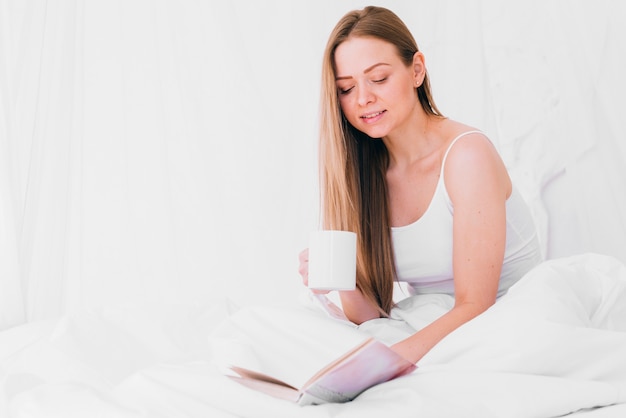 Mädchen, das Kaffee mit einem Buch auf dem Bett trinkt