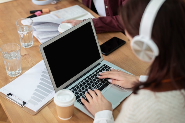 Mädchen mit Kopfhörern mit Laptop zusammen mit ihren Klassenkameraden während des Gruppenstudiums