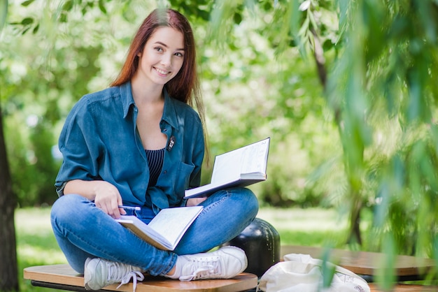 Kostenloses Foto mädchen sitzt auf dem tisch mit lehrbuch lächelnd