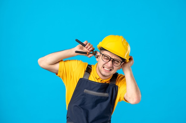 Kostenloses Foto männlicher arbeiter der vorderansicht in der uniform und im helm, die sein ohr auf blau schneiden