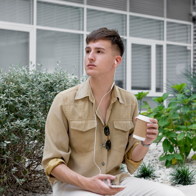 Kostenloses Foto mann, der draußen beim kaffee und beim hören auf musik auf kopfhörern aufwirft