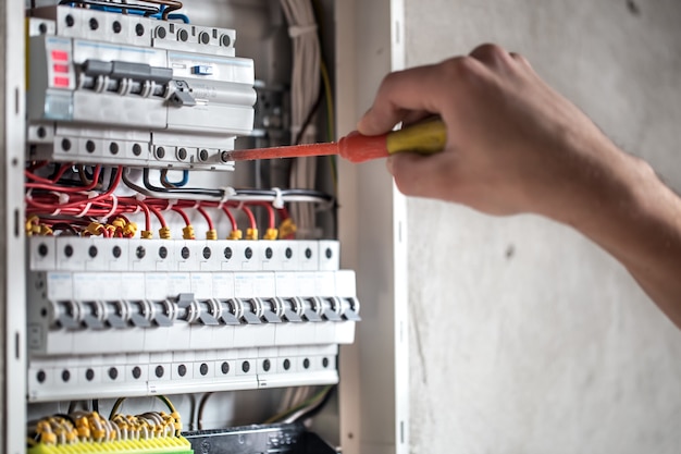 Kostenloses Foto mann, ein elektrotechniker, der in einer schalttafel mit sicherungen arbeitet. installation und anschluss von elektrischen geräten. nahansicht.