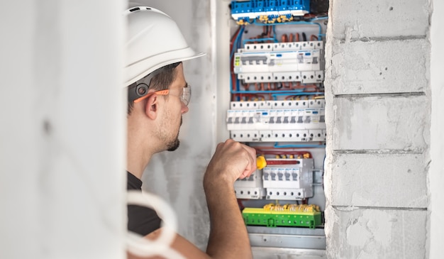 Kostenloses Foto mann, ein elektrotechniker, der in einer schalttafel mit sicherungen arbeitet. installation und anschluss von elektrischen geräten.