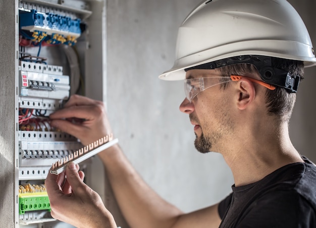 Kostenloses Foto mann, ein elektrotechniker, der in einer schalttafel mit sicherungen arbeitet. installation und anschluss von elektrischen geräten.