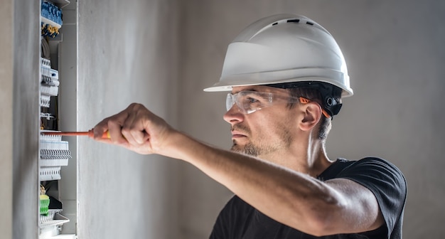 Kostenloses Foto mann, ein elektrotechniker, der in einer schalttafel mit sicherungen arbeitet. installation und anschluss von elektrischen geräten.