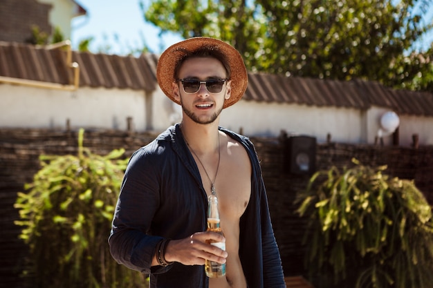 Kostenloses Foto mann in sonnenbrille und hut, der bier trinkt und im landhaus ruht