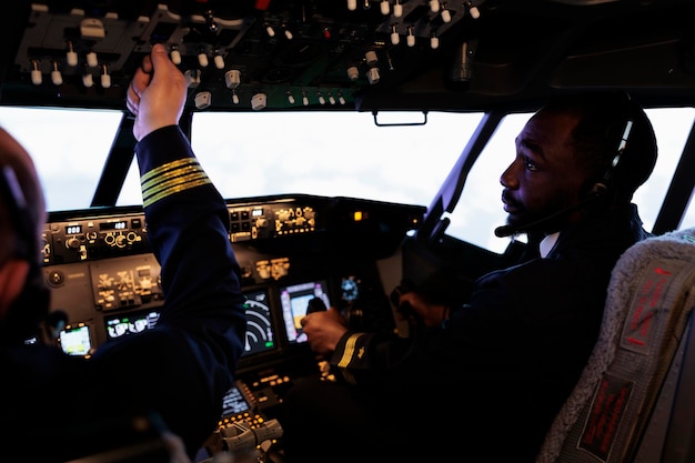 Kostenloses Foto multiethnisches team von piloten, die das bedienfeld im cockpit verwenden, um das flugzeug zu fliegen, den netzschalter und die befehlstasten auf dem armaturenbrett drücken, um abzuheben. internationaler airways-service mit flugzeugbesatzung in der kabine.