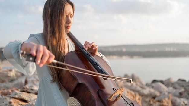 Kostenloses Foto musikerin, die cello bei sonnenuntergang mit kopienraum spielt