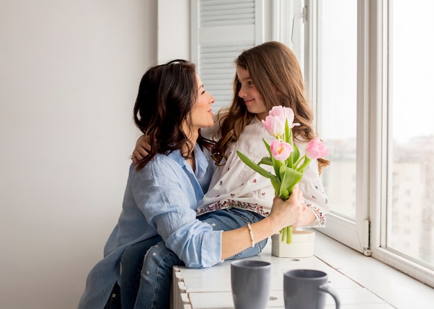 Kostenloses Foto mutter mit den tulpen, die tochter am fenster umarmen