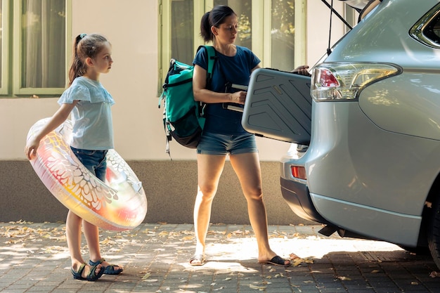 Kostenloses Foto mutter und kleines kind, die in den urlaub reisen, gepäckwagen und schlauchboot in den kofferraum des fahrzeugs laden, um während der sommerferien zum ziel am meer zu fahren. frau und kleines mädchen, die auf roadtrip abreisen.