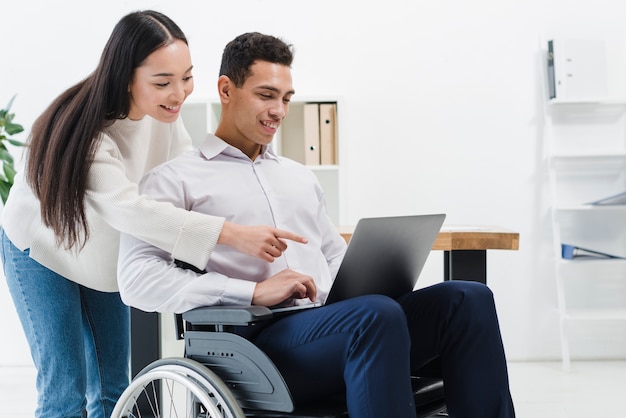 Kostenloses Foto nahaufnahme einer frau, die hinter dem geschäftsmann sitzt auf dem rollstuhl sitzt, der etwas auf laptop zeigt