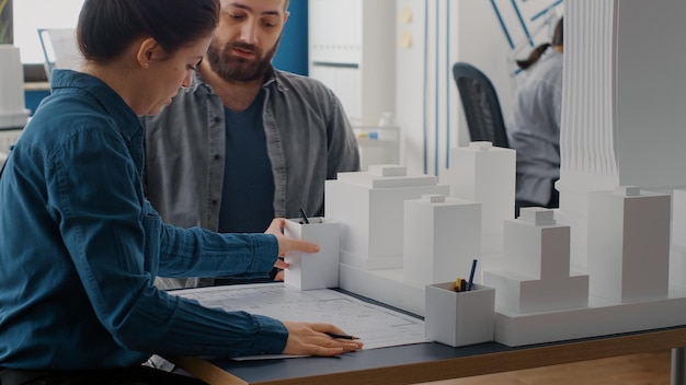 Kostenloses Foto nahaufnahme von mann und frau, die blaupausen entwerfen, gebäudemodell analysieren. team von leuten, die an baudesign mit industrieskizze und maquette für städtische projekte arbeiten.