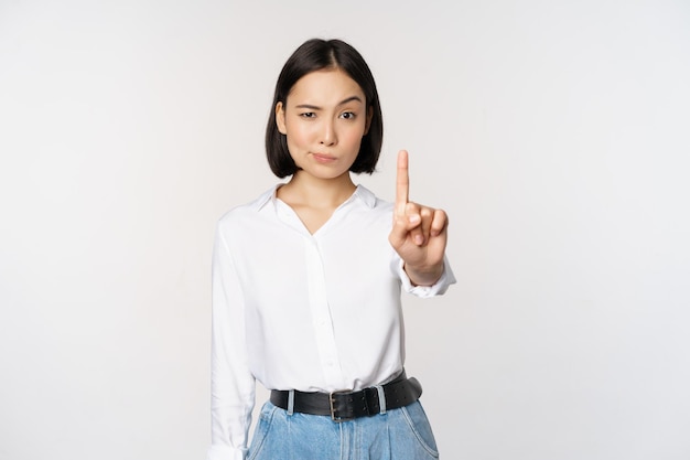 Kostenloses Foto nein junge ernsthafte und selbstbewusste asiatische frau, die ein tabu-schild mit einer fingergeste zeigt, das auf weißem hintergrund steht