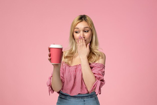 Nettes Mädchen schöne junge Dame mit rotem Lippenstift in rosa Bluse, die den Mund mit rosa Tasse bedeckt