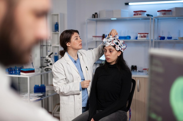 Kostenloses Foto neurologe-forscher-arzt, der den eeg-scanner am patientenkopf anpasst, der die gehirnentwicklung analysiert, die an der krankheitsdiagnose während des neurologie-experiments im high-tech-labor arbeitet. arzt erklärt tomographie