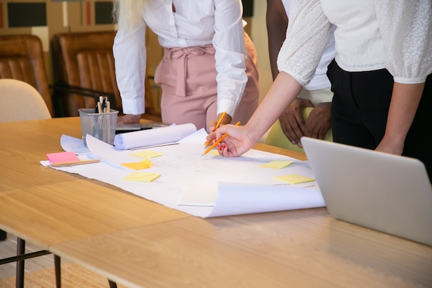 Kostenlose Foto nicht erkennbare designer, die auf ein großes blatt papier zeichnen und ideen austauschen