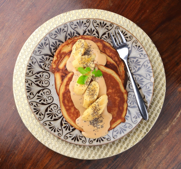 Kostenloses Foto pfannkuchen mit souse, bananen und chiasamen werden auf einem teller mit mustern serviert