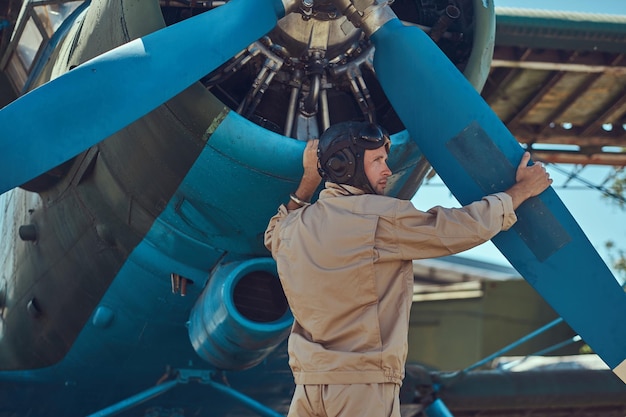 Kostenloses Foto pilot oder mechaniker in voller flugausrüstung überprüft vor dem flug den propeller seines retro-militärflugzeugs.