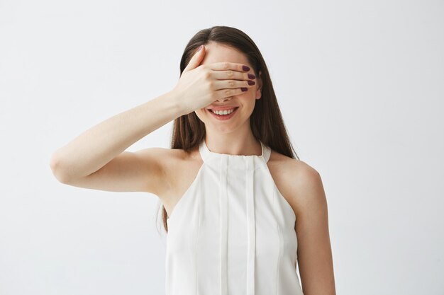 Kostenloses Foto porträt des jungen brünetten mädchens, das augen mit handlächeln bedeckt.