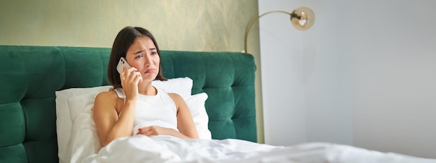 Kostenloses Foto porträt einer besorgten asiatischen frau, die ein mobiltelefon in der hand hält und einen schlechten anruf erhält, der besorgt und besorgt aussieht