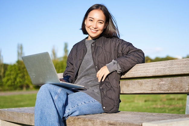 Kostenloses Foto porträt einer lächelnden frau, die mit laptop sitzt und an einem projekt arbeitet oder aus der ferne studiert und genießt, im park zu sein