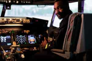 Kostenloses Foto porträt eines afroamerikanischen piloten, der dashboard-befehl in der kabine verwendet, um mit einem flugzeugjet abzuheben und zu fliegen. männlicher flieger in uniform der atemwege, der die tasten des bedienfelds und den leistungshebel drückt.