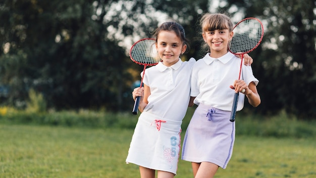 Kostenloses Foto porträt von zwei freundinnen, die mit badminton im park stehen