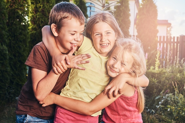 Kostenloses Foto portrait von glücklichen kleinen freunden, die sich am hof amüsieren. drei süße kleine freunde kuscheln und spielen.