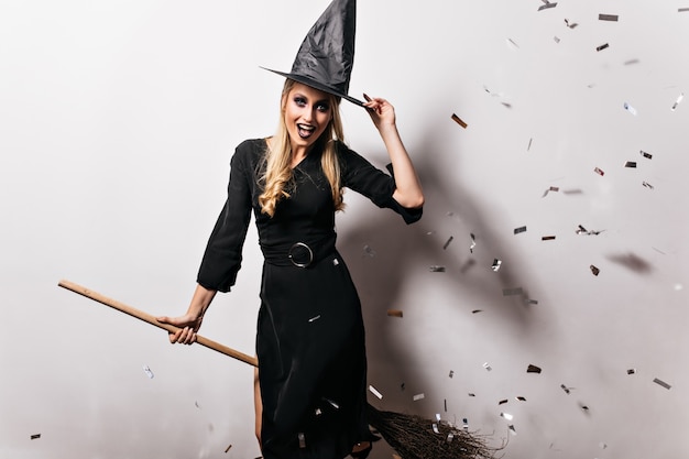 Kostenloses Foto raffinierte blonde frau, die im hexenkostüm posiert. hübsches kaukasisches mädchen, das spaß an der halloween-party hat.