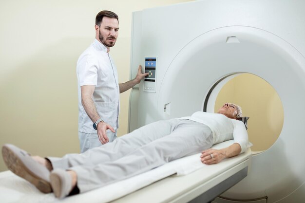 Reife Frau, die sich einem CT-Scan unterzieht, während der medizinische Techniker den Eingriff im Krankenhaus überwacht